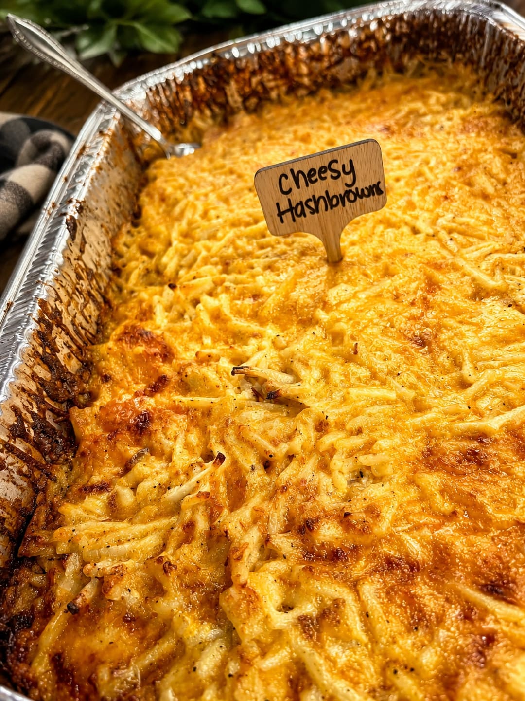 Maggie's Cheesy Hashbrowns in a catering tray with a hand-lettered wooden sign