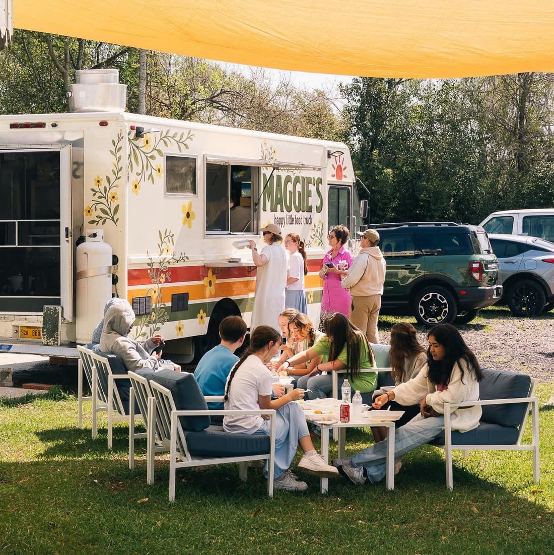 Maggie's flowery food truck at an event with guests eating under a sunshade